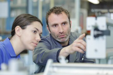 engineer teaching apprentice to use factory machine