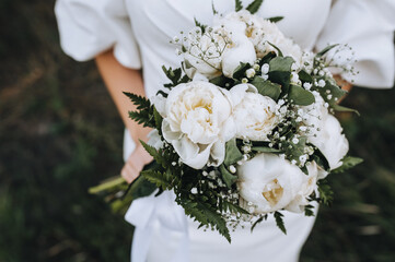 A beautiful bride in a white dress holds a bouquet of flowers, peonies close-up. Wedding photography.