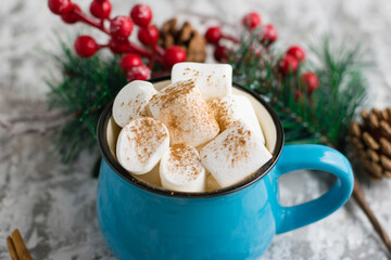 Obraz na płótnie Canvas Christmas cocoa drink with chewing marshmallows and cinnamon in a blue cup on a light background, close-up, top view