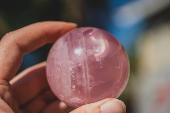 closeup of hand holding a rose quartz sphere with a rainbow