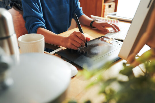 Close-up of unrecognizable designer sitting at table and working on new design using drawing tablet