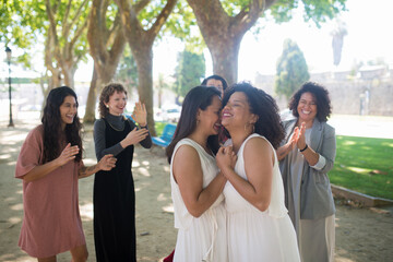 Joyful brides and guests dancing. Women of different nationalities in festive dresses laughing happily, applauding. Brides cuddling. Wedding, LGBT, celebration concept