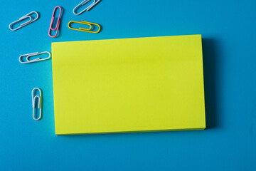 Top view of blank post-it note on blue background and different objects. Minimal flat lay style.