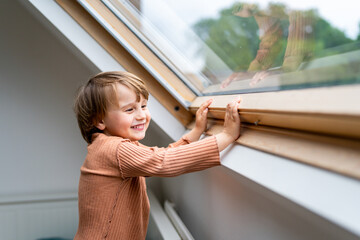 Close up portrait of a little preschool boy staying near  the window and laughing. Happy smiling...