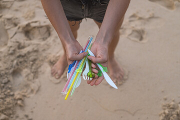 Hands holding used plastic dishes and straws on the beach. Sand on the background. Plastic pollution, Environmental Problem. Say no plastic. 