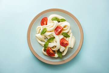 Traditional white soft fibrous Cecil cheese lies on a plate. The cheese is decorated with ripe tomatoes and basil, top view