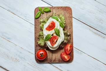 Homemade chechil cheese with fresh tomatoes, lettuce and basil leaves on wooden board, top view