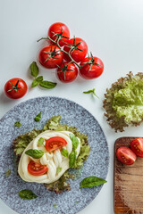 Traditional white soft fibrous Cecil cheese lies on a plate. The cheese is decorated with ripe tomatoes and basil, top view
