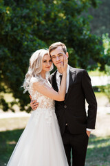 Naklejka premium Bride and groom at wedding day walking outdoors on summer nature. Stylish and beautiful. Bridal couple, Happy Newlywed woman and man embracing in green park. Loving wedding couple outdoor