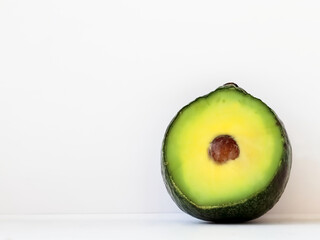 Half an fresh avocado on a table with a milky white wall as the background providing copy space on the left, close-up, front. Healthy food concept. Skin care, body treatment concept