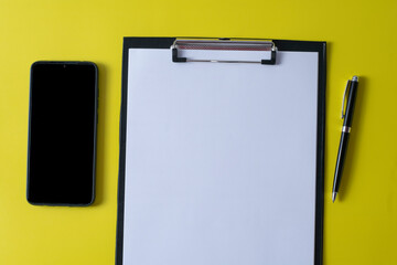 Top view of blank paper on clipboard on yellow background and different objects. Minimal flat lay style.