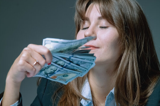 Portrait of pleased adult business woman sniffing US Dollar banknotes as symbol of earnings, income and savings the money. Horizontal image.
