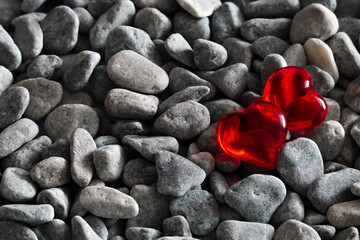Two red bright hearts among river pebble stones. The concept of passionate hearts of lovers among many lifeless stone hearts, different, uniqueness.