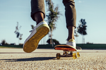 Closeup of black legs riding skateboard in park