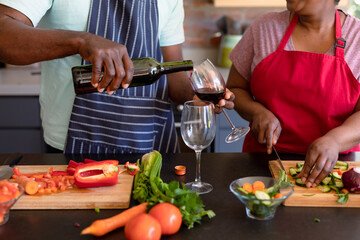 Midsection of african american senior couple cooking together in kitchen, drinking wine