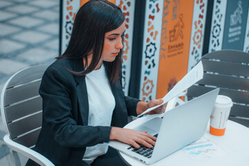 Señorita joven de pelo castaño revisando contratos de trabajo de sus empleados en una cafetería...