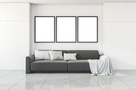 Grey sofa in white living room interior with mockup frames