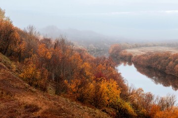 View from the hill to the river with autumn trees along the banks. Foggy morning