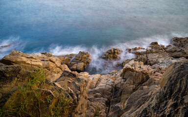 Fototapeta na wymiar Top view of the rocky coast with vegetation, waves breaking against cliff at sunset and silk effect, Blanes, Catalonia, Spain