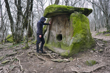 Fototapeta na wymiar Tourist (man) looking at dolmen Mother's heart in Pshada village on cloudy winter day. Krasnodar Krai, Caucasus, Russia.