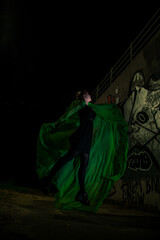 Naklejka premium Girl posing in green draping on dark background