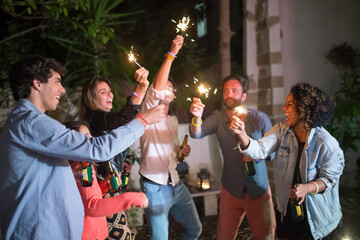 Young men and women partying at backyard. Group of males and females of different nationalities holding beer bottles, lighting sparklers. Party, celebration, nightlife concept