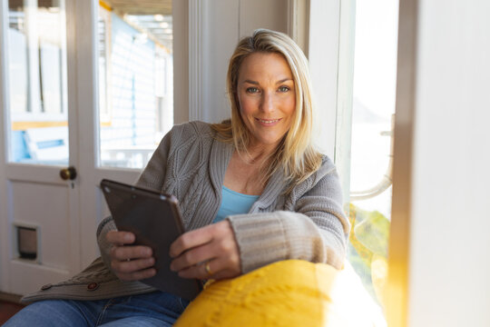 Happy caucasian mature woman using tablet in sunny living room