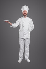 Cheerful chef in uniform holding empty plate