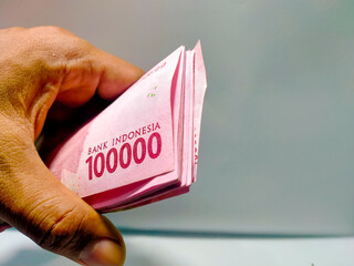 The hand is holding the hundred thousand rupiah denomination on the left side of the background for the giveaway prize