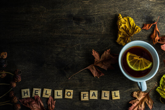 Cup of lemon tea on a table with autumn leaves and the words Hello Fall