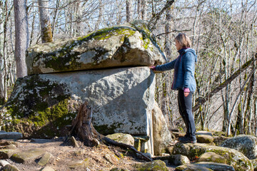 A tourist (young woman) standing nearby ancient dolmen in Zhane river gorge on sunny winter day. Krasnodar Krai, Russia.