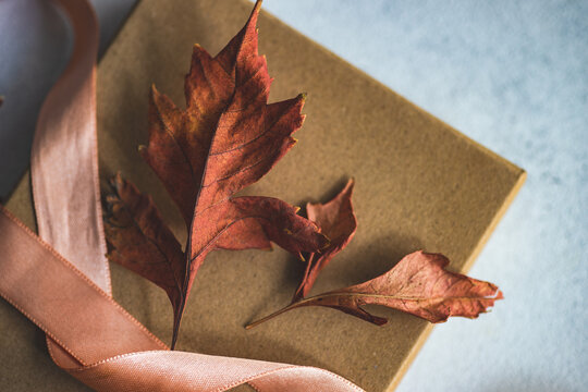 Close-up of an Autumnal gift box tied with a ribbon and dried autumn leaf decorations on a table