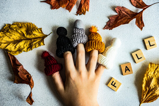 A hand with fingers wearing woolly hats and the word fall spelled in wooden blocks with autumn leaves