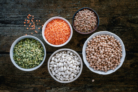 Overhead view of bowls of assorted raw legumes on a wooden table