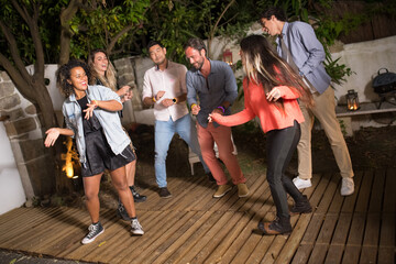 Young men and women dancing at backyard. Group of males and females of different nationalities partying outdoors, smiling, talking. Party, celebration, nightlife concept