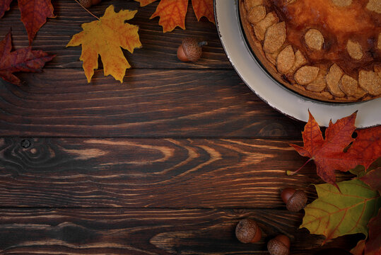 Autumn background with pumpkin cake, maple leaves, aples and acorns. Top view. Copy space