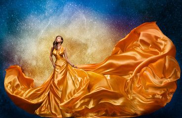 Fashion Model in Golden Dress over Miracle Night Sky Background. Luxury Woman in Long Silk Gown...