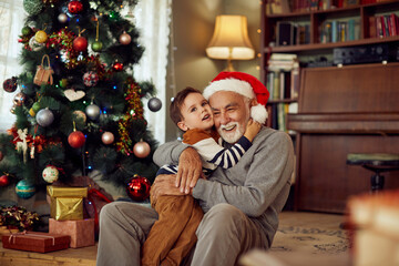 Happy grandfather and grandson embrace on Christmas day at home. - obrazy, fototapety, plakaty