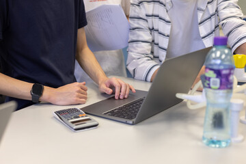 group of young university students or business people discuss, work together, note some data on notepad, laptop computer, tablet, mobile phone on desk in classroom, office or laboratory