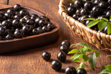 Jabuticaba, Jabuticabas freshly harvested and not yet washed, placed in a straw basket and wooden bowl on rustic wood, selective focus.