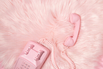 Pastel pink retro telephone handset and pastel pink faux fur background. Vintage aesthetic 80s or 90s fashion background. Romantic communication idea.