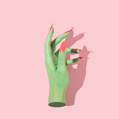Halloween creative concept with green witch hand with bright pink nails against pastel pink...