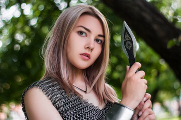 Close-up portrait of a girl in chain mail armor with a spear in her hands on the background of the...