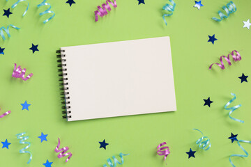 Open notebook, colorful serpentine and stars, on green  background. Flat lay, top view, copy space.