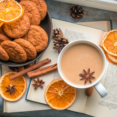 A large cup of coffee and a book near the window, several knitted blankets and slices of dried oranges remind of autumn, a cozy time and home holiday. Flat lay