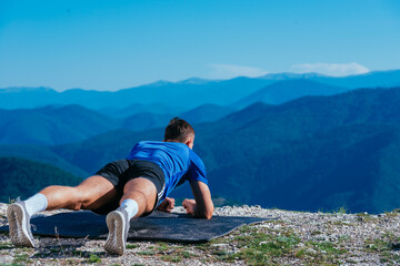Naklejka premium Strong male athlete doing plank while exercising his abs on top of a mountain on a sunny day.