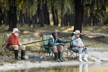 Multiethnic elderly men with fishing rods spending time near lake - Powered by Adobe