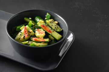 Asian spicy broken Cucumber salad with fresh coriander, ginger, pepper chili, black vinegar on black background. Spicy cucumbers. Popular Chinese appetizer. Close up.