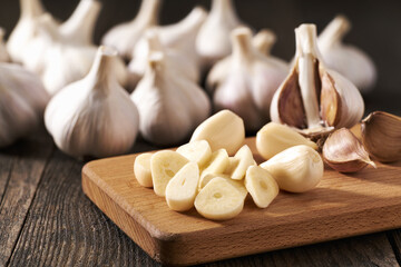 Chopped garlic on a cutting board, in background a pile of garlic unpeeled.