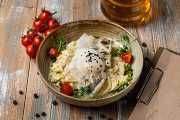 A stylized photo of fish and potato gratin with rich creamy sauce, wooden table with spices and tomatoes laying around